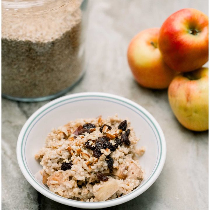 A bowl of Overnight Steel Cut Oats with apples in the background